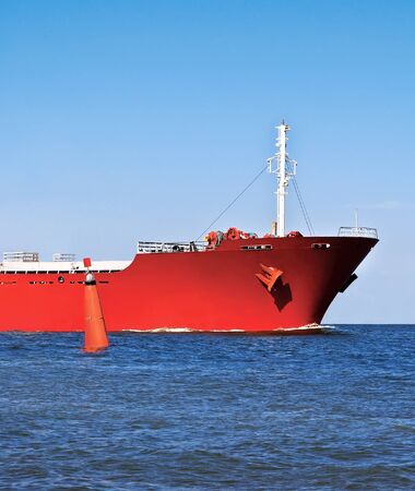 Bow of the red cargo ship in the ocean and a red buoy.の写真素材