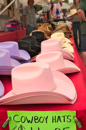 Colorful cowboy hats on display and for sale at a county fair with blurred shoppersの写真素材