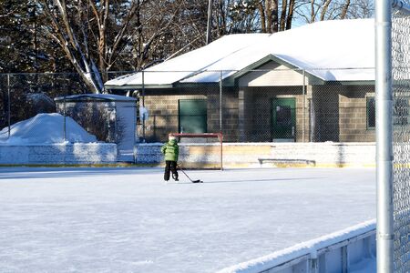 Outdoor ice hockey rink in late afternoon with a single skater practicing his shot.の写真素材