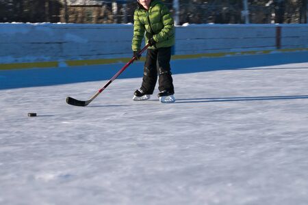 Outdoor ice hockey rink in late afternoon with a single skater practicing his shot.