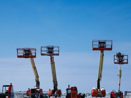 Telescopic Boom Lifts in snowy winter storage area with blue sky.