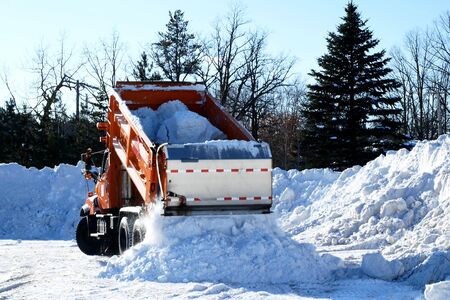 Orange dump truck empties a load of snow after several winter snow storms in Minnesota.