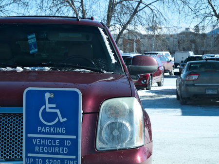 BEMIDJI, MN - 27 FEB 2019: Handicapped parking sign posted in snow covered parking lot and red car with handicapped placard in window.のeditorial素材
