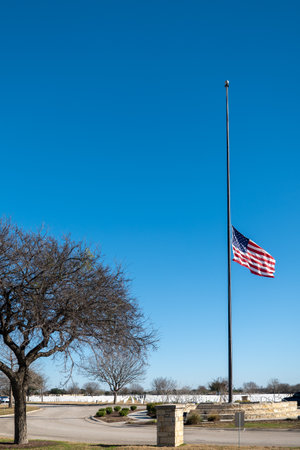 SAN ANTONIO, TX - 23 JAN 2020: US flag at half mast in military cemetery at Fort Sam Houston under blue sky with grave markers in distance.のeditorial素材