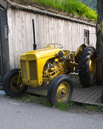 GEIRANGER, NORWAY - 15 JUN 2019: Vintage Yellow Tractor parked next to building with green grass turf roof.のeditorial素材
