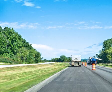 A truck drives by orange warning barrels on asphalt highway at a utility work site on a sunny day.