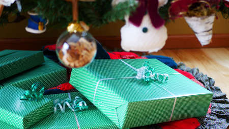 Christmas gifts wrapped in green paper and ribbon, piled under the Christmas tree, with some...