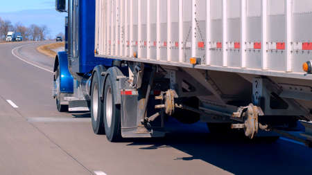 Semi truck and trailer driving on an American freeway on a sunny day, as seen through the windshield...