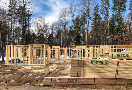 House construction site with wall studs and stacks of wood trusses on the ground, ready for...