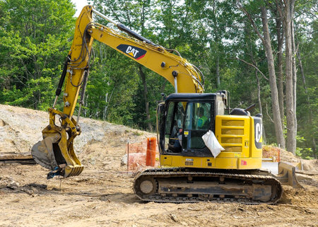 CASS CO, MN - 6 AUG 2021: Caterpiller or CAT excavator with hydraulic scoop working at a construction site in forest with trees.のeditorial素材