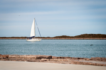 A white Sailboat, sailing left to right on the blue water of the shipping channel to the Gulf of Mexico in Port Aransas, Texas.の写真素材