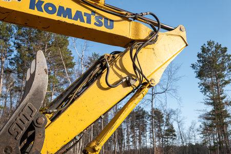 CROW WING CO, MN - 3 MAY 2023: Komatsu Excavator boom arm elbow and hydraulics tubing on a working heavy equipment machine, on a new home construction site, with blue sky and trees in the background.のeditorial素材