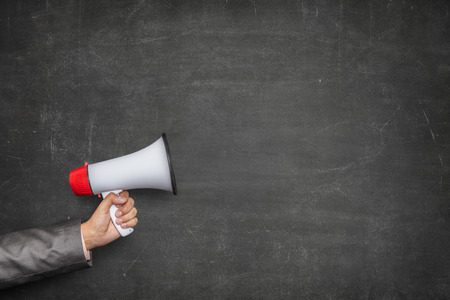 Businessman hand holding megaphone on front of vintage full frame black blank blackboard no frameの写真素材