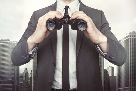 Businessman holding binoculars with tie and shirt on cityscape backgroundの写真素材