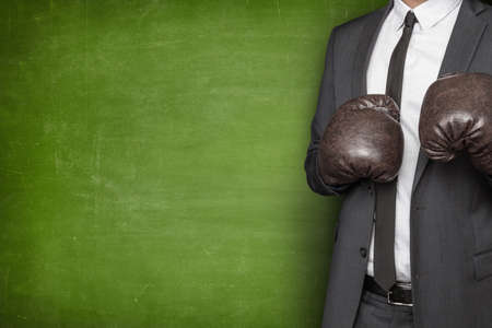 Businessman in boxing gloves and suit on blackboard backgroundの写真素材