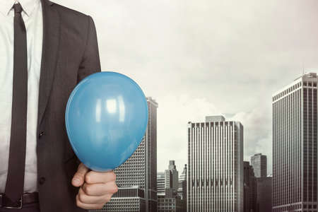 Businessman holding balloon in hand in suit on cityscape backgroundの写真素材