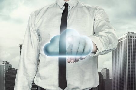 Cloud computing concept with businessman on cityscape background pointing towards blue cloudの写真素材