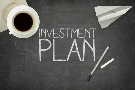 Investment plan concept on black blackboard with coffee cupt and paper plane