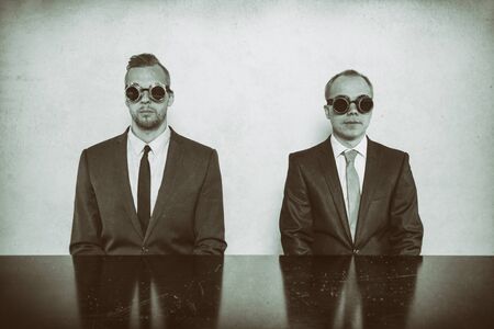 Two businessman sitting at office desk wearing glassesの写真素材