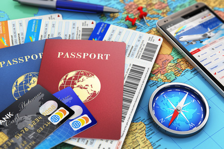 Creative abstract business travel and tourism concept: air tickets or boarding pass, passports, touchscreen smartphone with online airline tickets booking or reservation internet application, magnetic compass, credit cards and pen on world geographic map Creative abstract business travel and tourism concept: air tickets or boarding pass, passports, touchscreen smartphone with online airline tickets booking or reservation internet application, magnetic compass, credit cards and pen on world geographic map