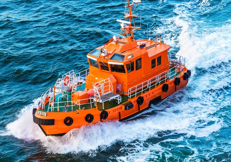 Orange rescue or coast guard patrol boat industrial vessel in blue sea ocean waterの写真素材
