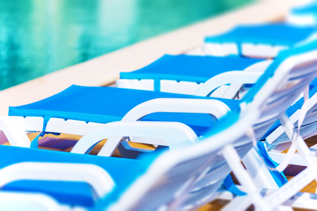 Creative abstract travel, tourism and summer vacation holidays activity concept: macro view of chaise longue beach chairs and swimming pool with blue water in tropical spa resort hotel with selective focus effectの写真素材