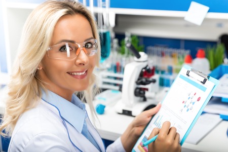 Young happy smiling attractive woman scientist in protective eyeglasses researching in the...