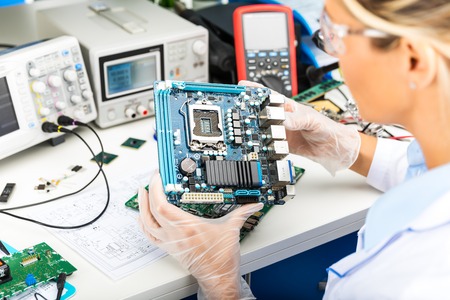 Young female digital electronic engineer examining computer PC motherboard in laboratory