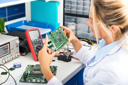 Young attractive female digital electronic engineer checking green circuit board PCB in laboratory