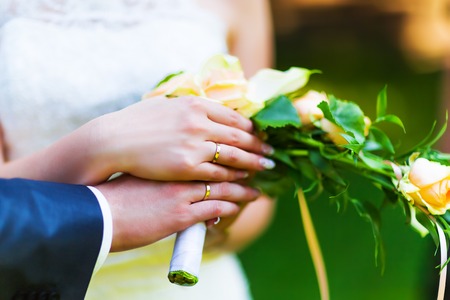 Macro view of the hands of married couple of bride and groom with golden wedding rings with selective focus effectの写真素材