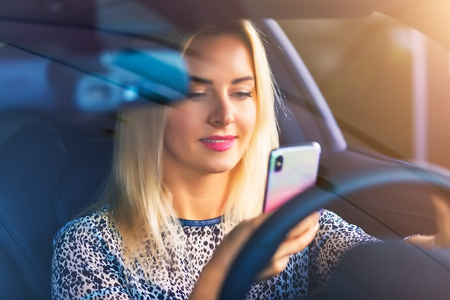 Young smiling woman driver using a smartphone in the modern luxury carの写真素材