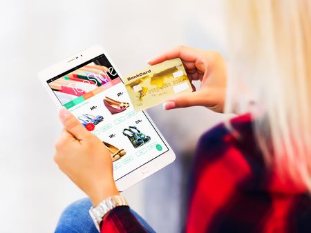 Young blonde woman with long hair shopping online with tablet computer and credit card in the fashion store and making purchase and paymentの写真素材