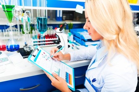 Young happy smiling attractive woman scientist in protective eyeglasses researching in the scientific chemical laboratoryの写真素材