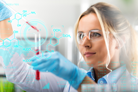 Young attractive female scientist researching in the laboratory with futuristic scientific air interface with chemical formulas and research data in the foregroundの写真素材
