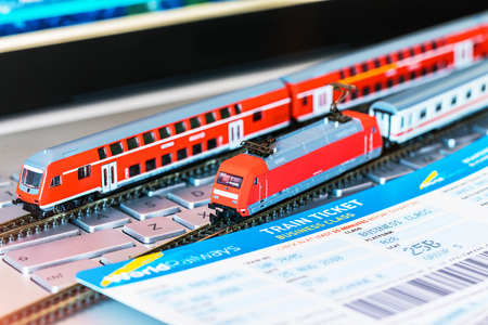Red toy passenger train, railway travel tickets, passport, bank card and eyeglasses on laptop or notebook computer PC with selective focus effectの写真素材