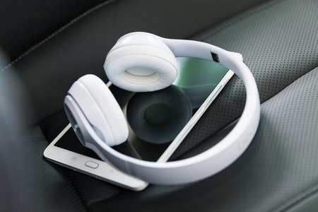 Modern wireless internet technology concept: macro view of tablet computer PC and white wireless headphones on the black leather car seat with selective focus effectの写真素材