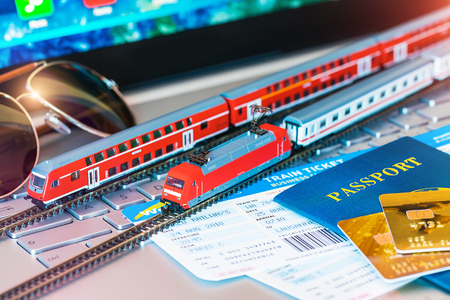 Red toy passenger train, railway travel tickets, passport, bank card and eyeglasses on laptop or notebook computer PC with selective focus effectの写真素材