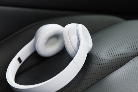 Modern wireless internet technology concept: macro view of the white wireless headphones on the black leather car seat with selective focus effectの写真素材