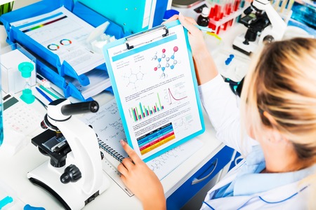 Young happy smiling attractive woman scientist in protective eyeglasses researching in the scientific chemical laboratoryの写真素材