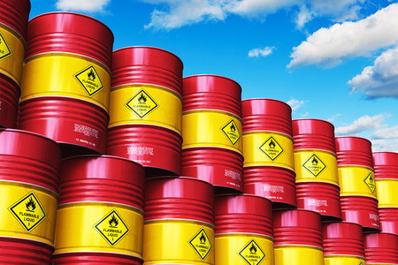 Creative abstract oil and gas industry manufacturing and trading business concept: 3D render illustration of the industrial storage warehouse with the group of stacked rows of red metal oil drums or petroleum barrels against blue sky with cloudsの写真素材