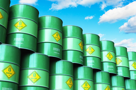 Creative abstract ecology, alternative sustainable energy and environment protection saving business concept: 3D render illustration of the group of green stacked metal biofuel drums or biodiesel barrels in the industrial storage warehouse against blue sky with cloudsの写真素材