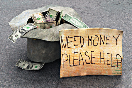 Macro view of the homeless poor beggar's hat with dollar money cash banknotes and the help message on the piece of cardboard on the street road asphalt outdoorsの写真素材