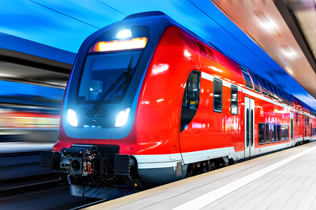 Creative abstract railroad travel and railway transportation industrial concept: modern red high speed electric passenger commuter double deck train at the illuminated station platform at night with motion blur effectの写真素材