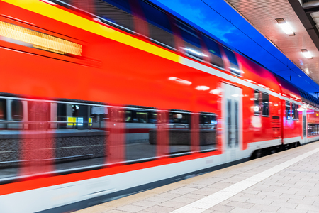Creative abstract railroad travel and railway transportation industrial concept: modern red high speed electric passenger commuter double deck train at the illuminated station platform at night with motion blur effectの写真素材