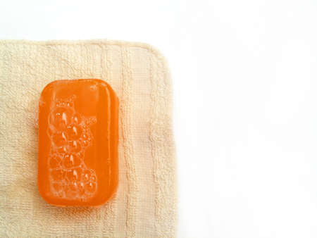 Orange bar of semi-transparent soap on a beige/tan colored dry washcloth.の写真素材