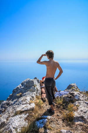 An unknown hiker (adventurer) is standing on the cliff is looking at the vast blue ocean and mountain under a big blue sky. Crimeaの写真素材