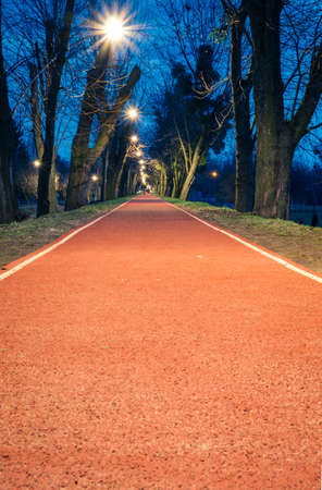 Red running lane in a public park in the evening. Running red road in the park in early spring eveningLutsk, Volyn, Ukraine.の写真素材