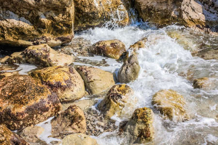 The waves breaking on a stony beach, forming a spray. Close upの写真素材