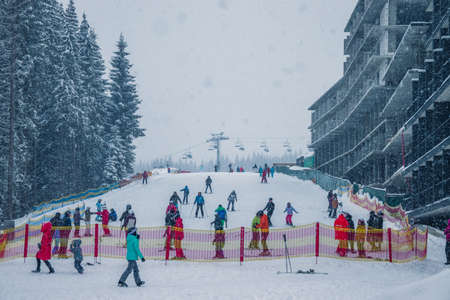 Ukraine. Bukovel - 02 FEBRUARY 2021. Ski lift with skiers and christmas trees. Skiers on the slide. Part of the lift up the mountain, winter cloudy day with snowfall.のeditorial素材