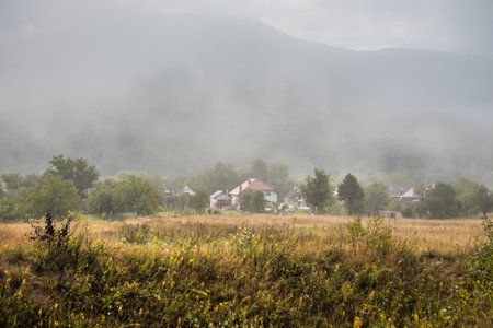 Mountain from view with small village and flow fog. Foggy summer morning in the mountains and a small village. Country road in the mountains. Carpathians. Polyana. Ukraineの写真素材
